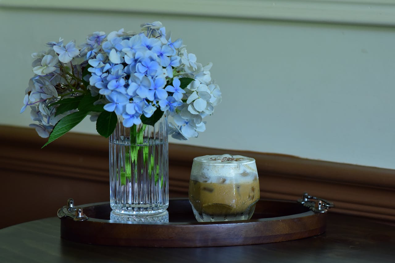 Stylish floral arrangement with iced coffee on a wooden tray, perfect for a serene indoor setting.